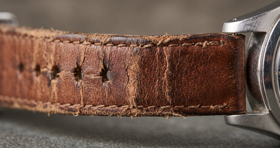 Worn brown leather watch strap with cracks and stretched holes, ready to be replaced
